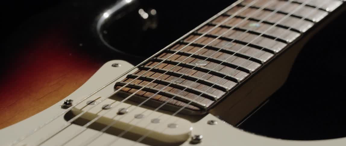 An electric guitar with a white body and wood neck is sitting on a wood table