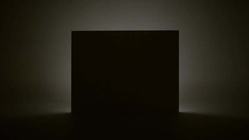 A light shines from behind a silhouetted box in the dark