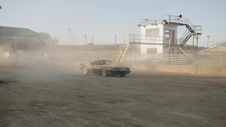 A car driving in a stadium raising dust