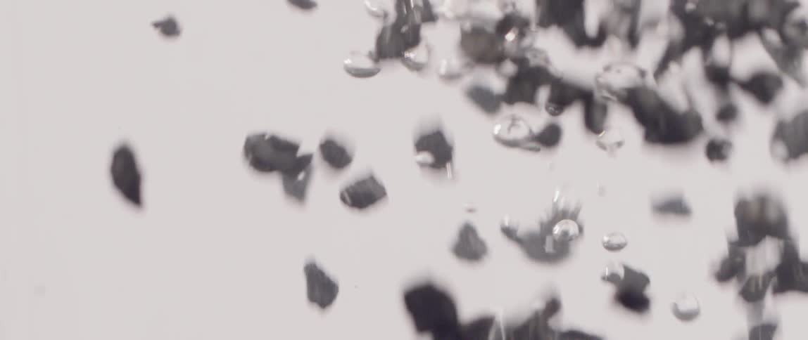 Small silver chucks of solid material are dropped in a clear liquid