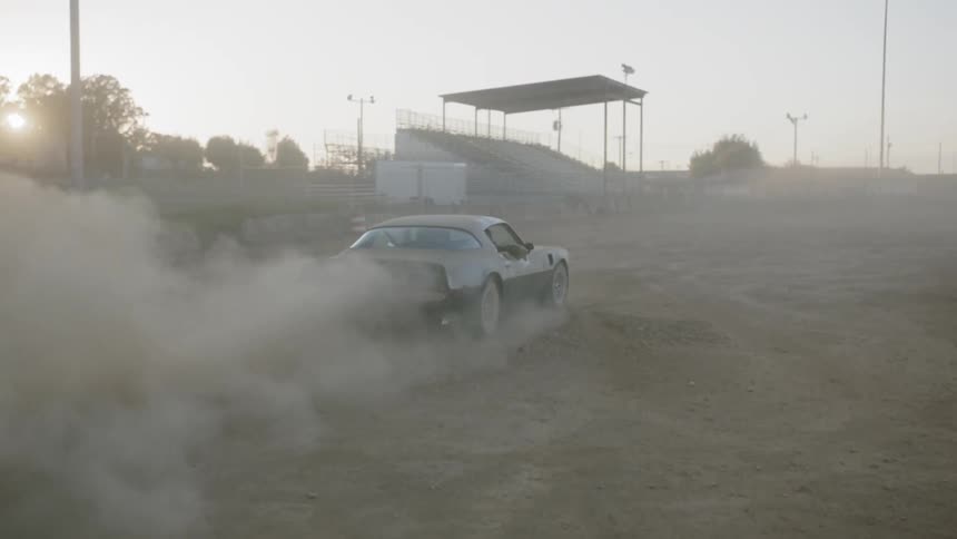 A black muscle car is kicking up dust on a dirt arena