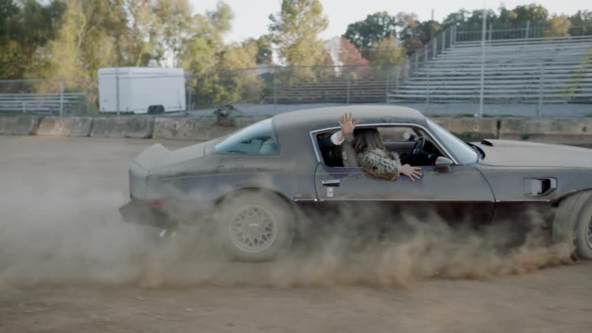 Two men and a woman in expensive clothing making a sharp turn in a sports car causing a cloud of dust to hide the car