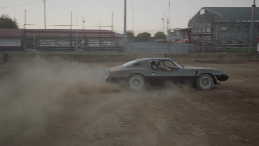 A black muscle car spins a cookie in a dirt arena