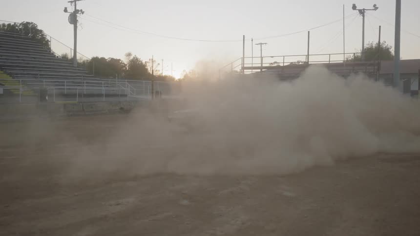 A muscle car in a stadium driving and raising dust