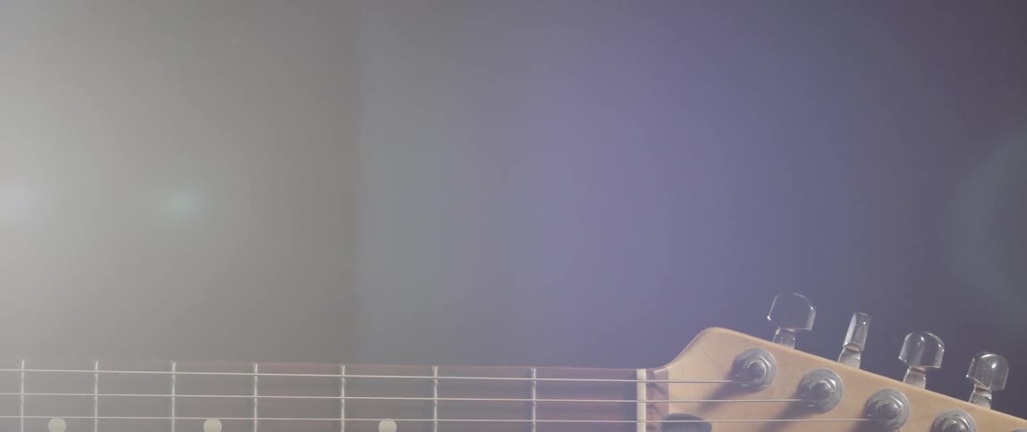 A light shines behind the neck of a guitar
