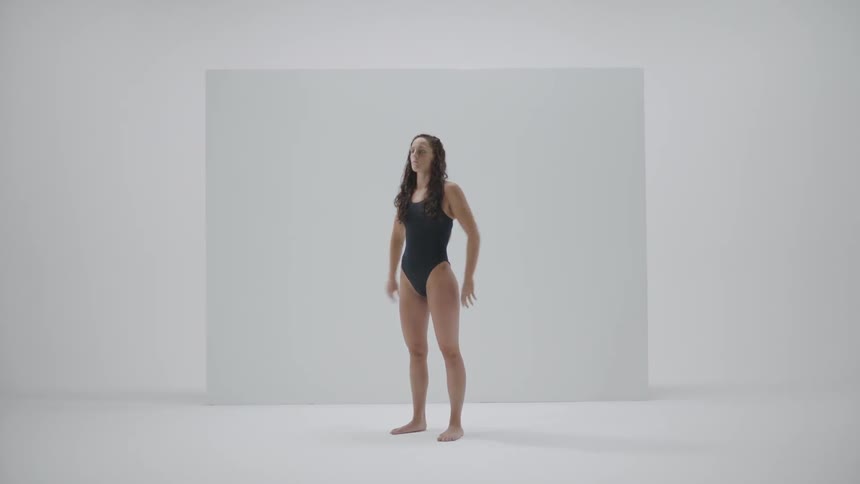 A woman wearing a bathing suit stands in an empty room and stretches