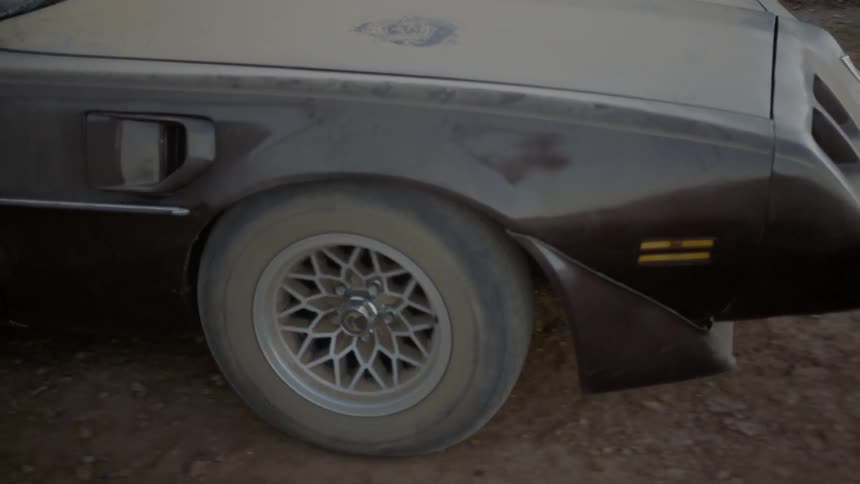 A black muscle car covered in dust drives slowly forward