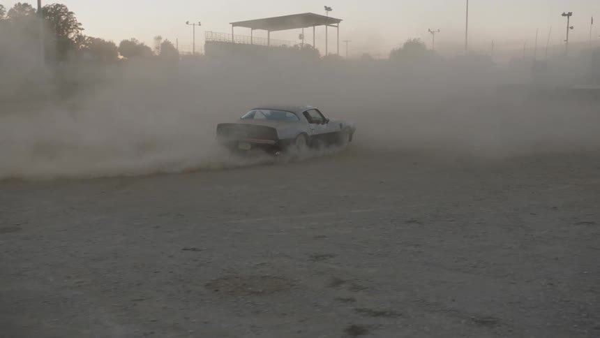 The car is drifting in the dirt making dust clouds