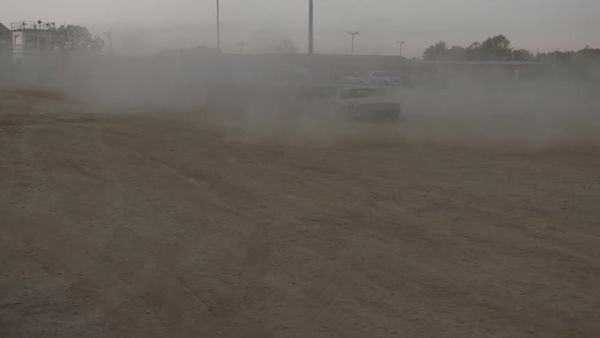 A sports car can be seen driving haphazardly through a dirt field while creating clouds of dust everywhere
