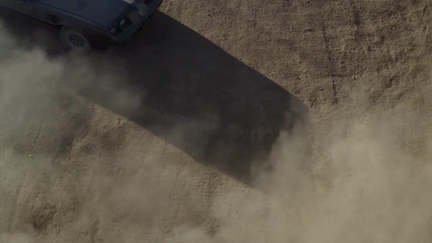 A car kicks up dust while spinning cookies in a dirt field