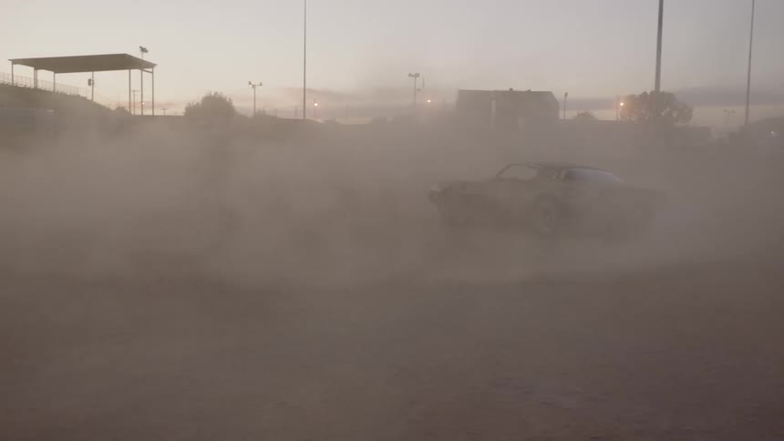 A sports car doing donuts in a fog of dust
