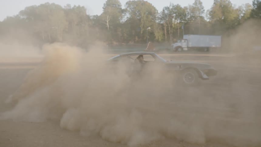 A car kicks up dust as it does donuts on a dirt track