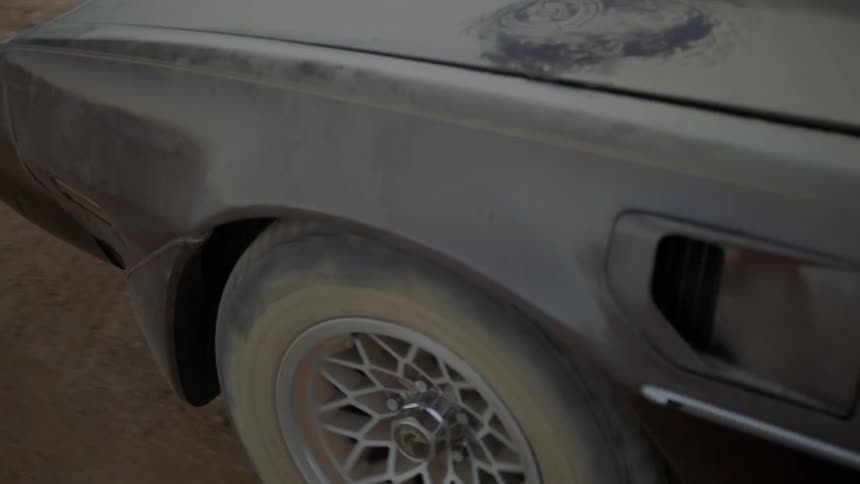 A dust covered muscle car travels on a dirt road