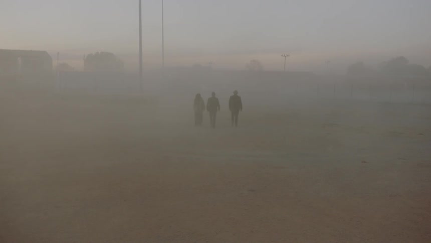 Three people walk through a field enveloped in fog