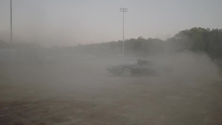 An old sports car does burn outs in a dirt track stadium