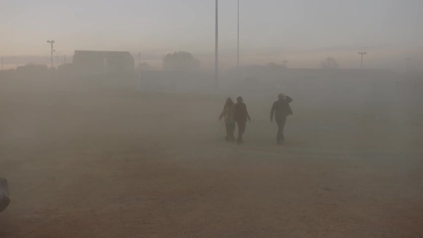 Three people walk through a park filled with smoke