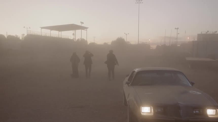 Three people walk past a vehicle in dense smoke of a parking lot