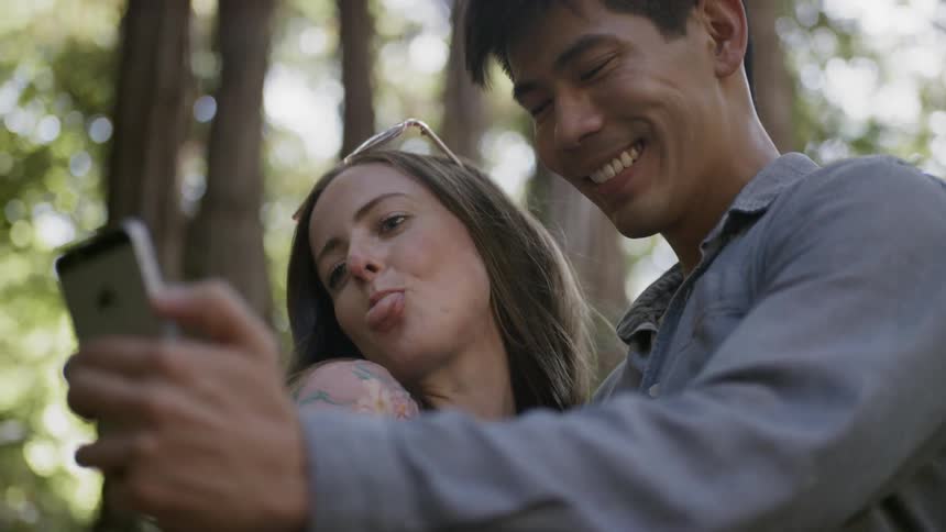 A man and a woman taking a picture with a smart phone in the forest