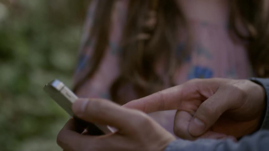 A man standing next to a woman is holding a cellphone and pointing at it