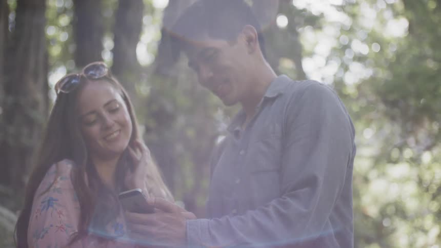 A man shows a woman something from his phone while they are standing in the woods