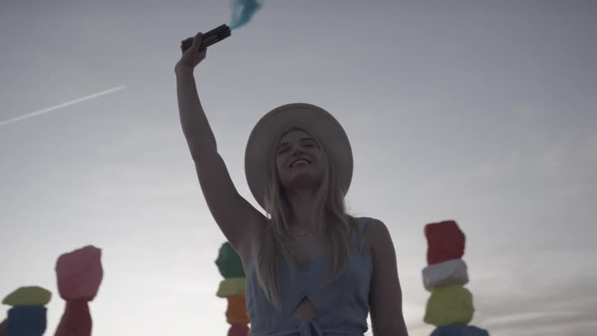 A woman with a sun hat holding a blue smoke flare