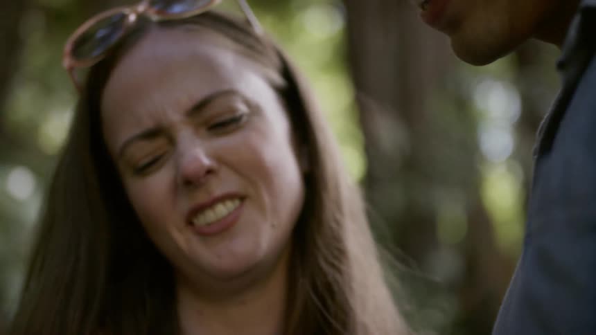 Asian man and white woman look down and talk with each other in the forest during daylight