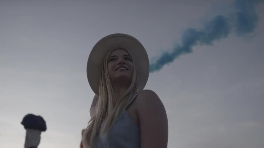 A woman holds a blue smoke bomb behind her