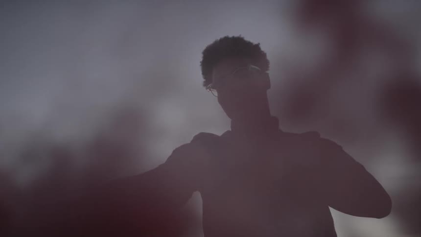 Man playing with a colored smoke bomb in desert at sunset