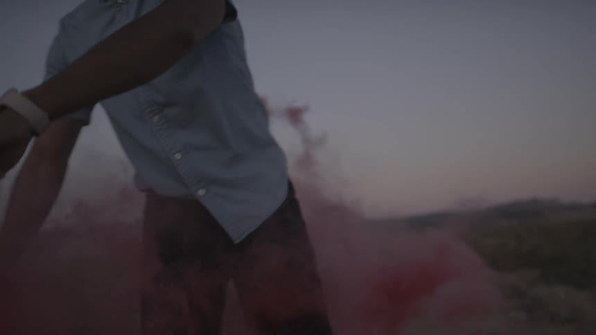 A young man playfully waving a violet smoke flare in the desert
