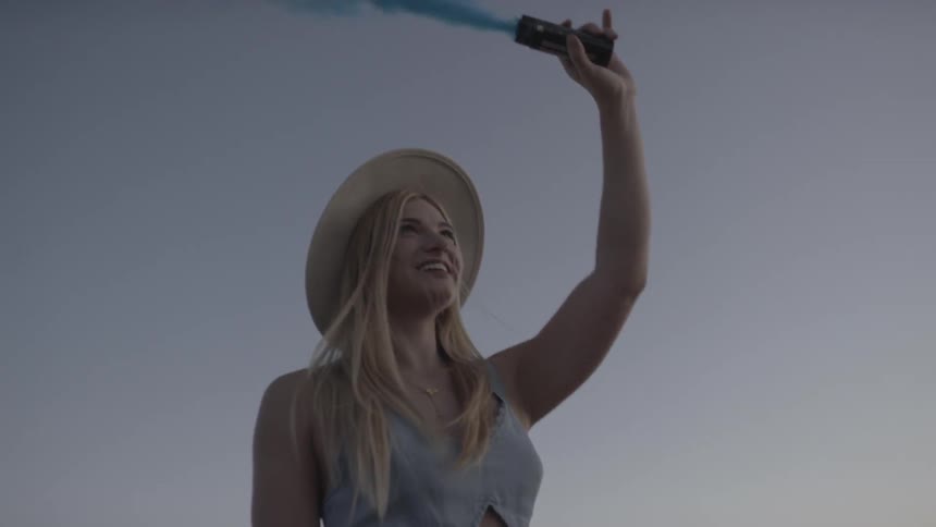 A blonde female holding up a blue flare at a festival