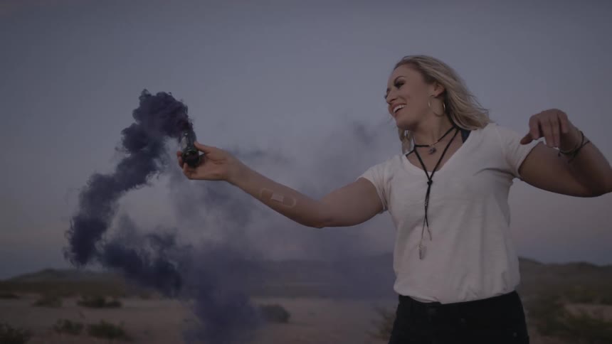 A blonde female holding up a blue flare at a festival