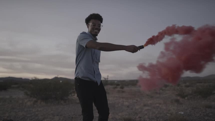 A man playing with a purple smoke flare in the desert