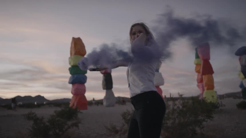 A blonde woman spins around while holding a smoke grenade