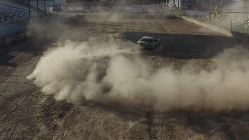 A muscle car doing donuts in the dirt with dust billowing