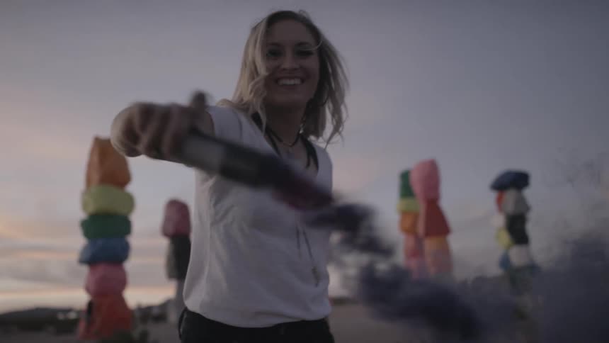 A woman smiles while waving around a burning flare outside at sunset