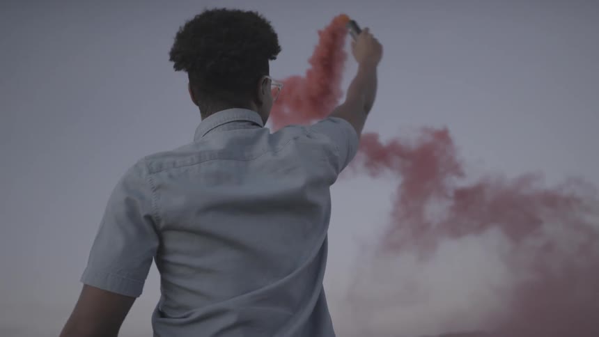 A smiling man holds up a red smoke stick and turns round and round