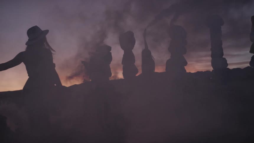 A group of people wave smoke around a display of large stacked rocks