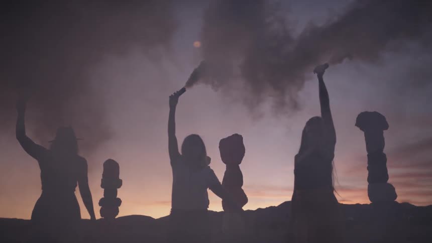 People stand outside with their arms raised above their heads while holding tubes with smoke coming out of them