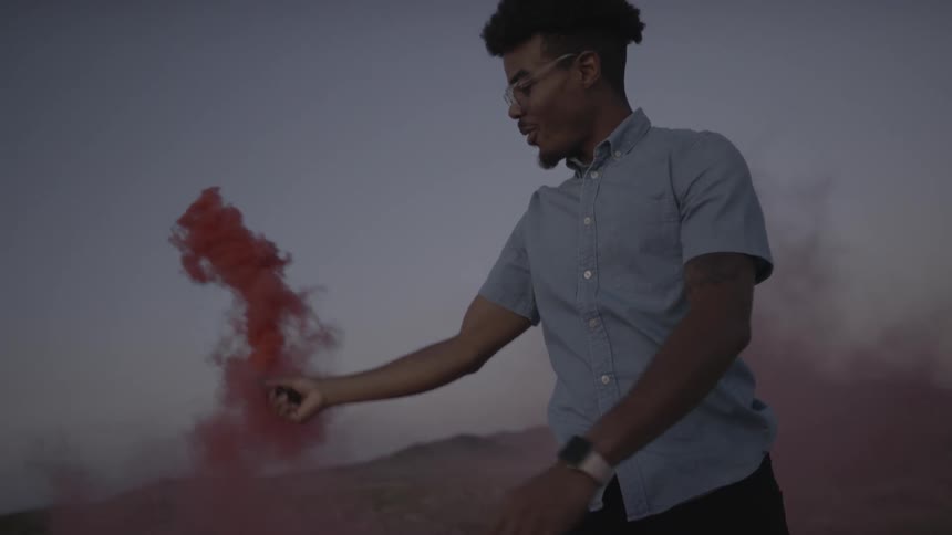 A man in the desert waving a red smoke flare