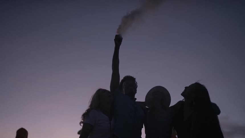 A group of people hug in the desert while holding a smoke bomb aloft