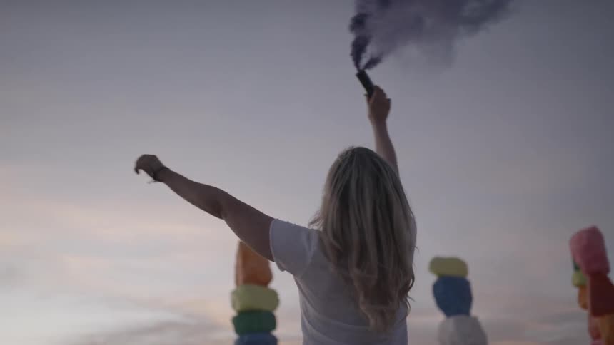 A blonde female holding up a blue flare at a festival