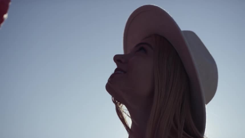 A woman with blonde hair wears a sun hat and looks at installations
