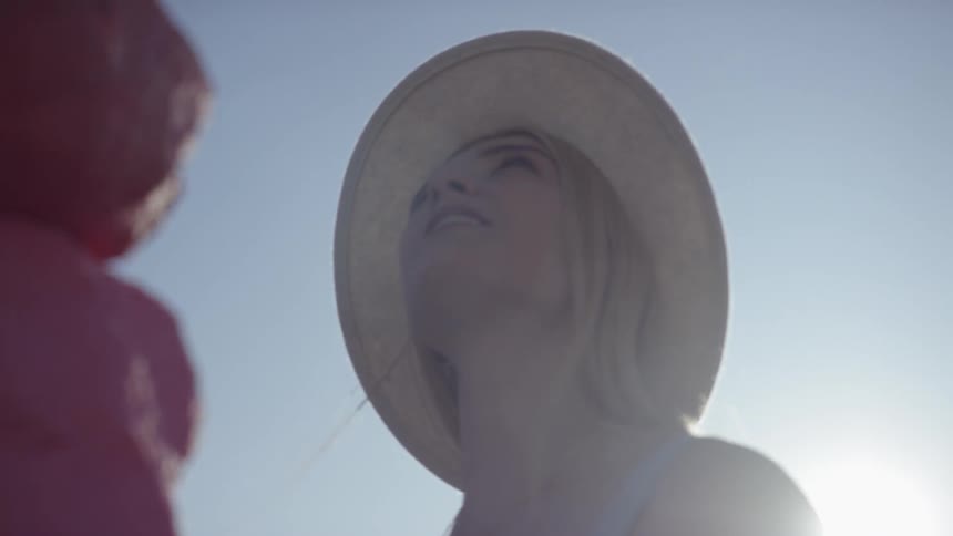 Blonde woman wearing wide hat looks around while the sun shines behind