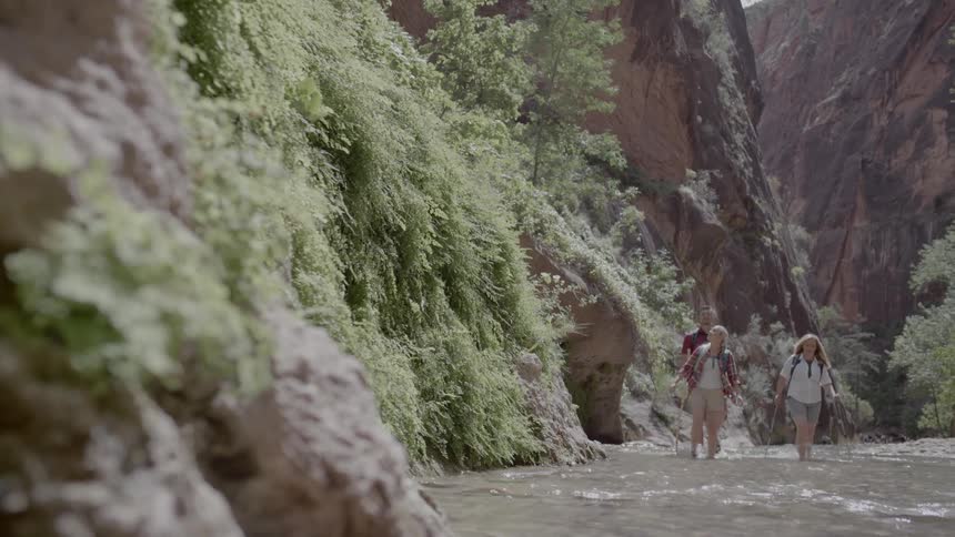 Man and two women walk along the stream between the two mountains on a sunny day