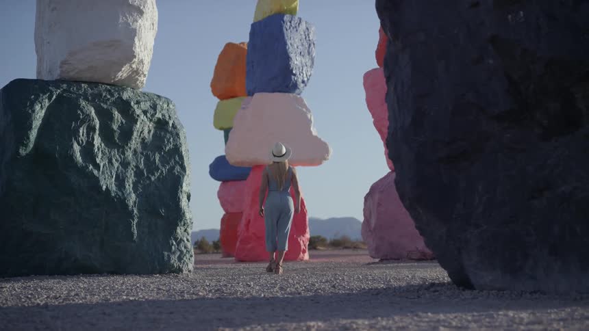 A woman with blonde hair wears a sun hat and looks at installations