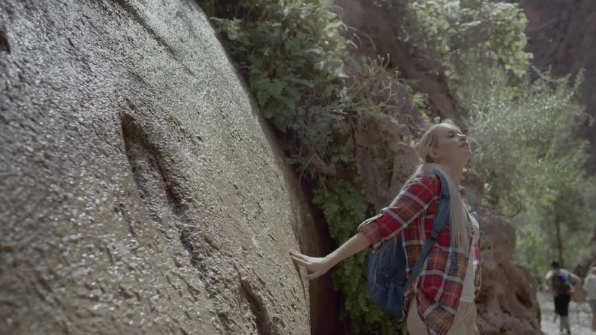 A woman stands near a large rock