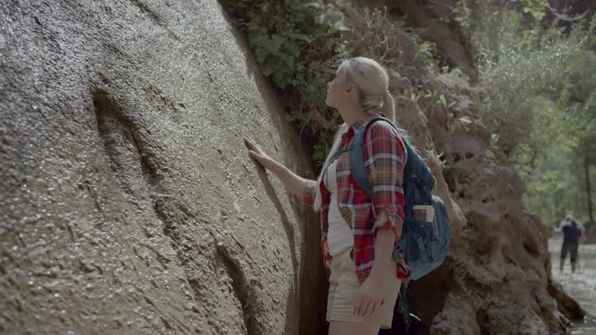 Woman hiking on a shallow river standing near boulder