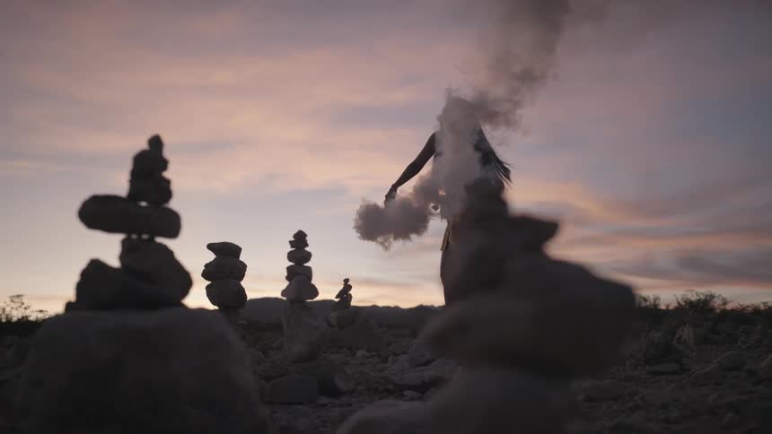 Woman dancing with a smoke bomb surrounded by balanced rocks at sunset