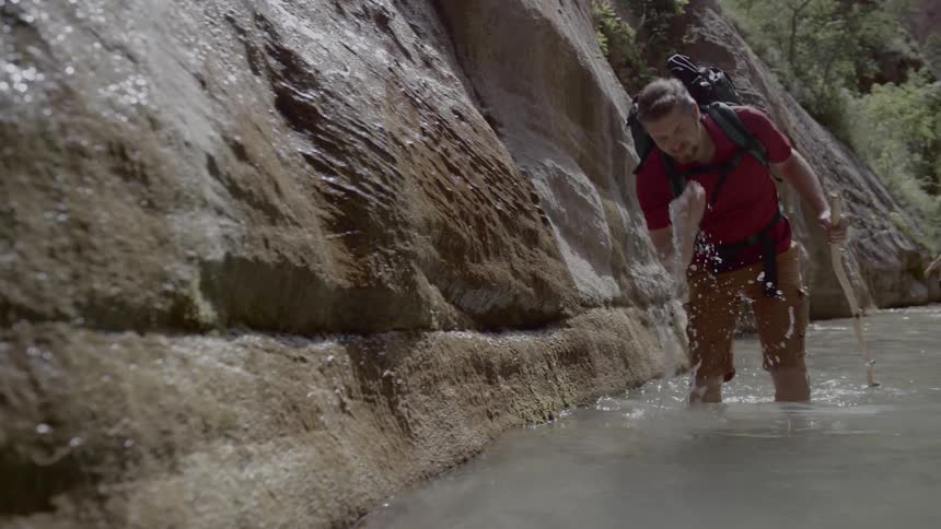 A man hiking through a river bends over and splashes water on his face