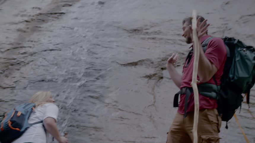 A woman splashes a man with water that is running down a cliff